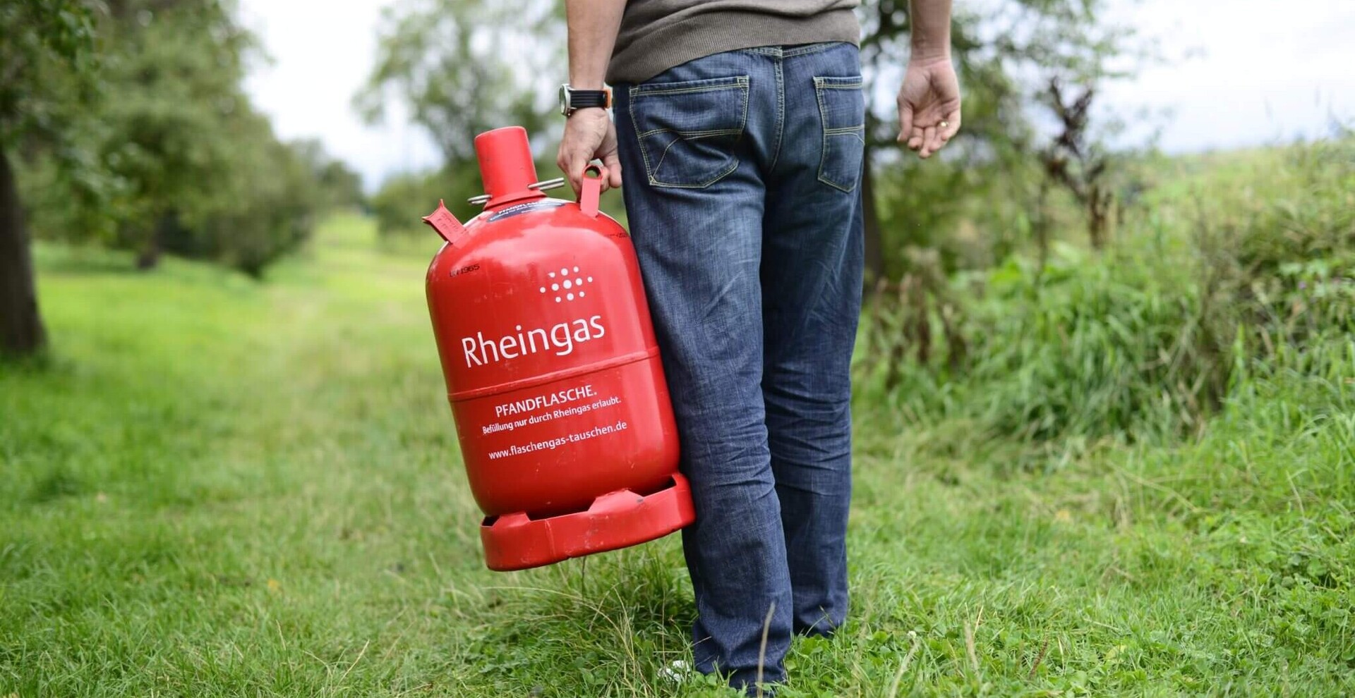 Mann trägt 11 kg Gasflasche zum Grillplatz über einen Feldweg.