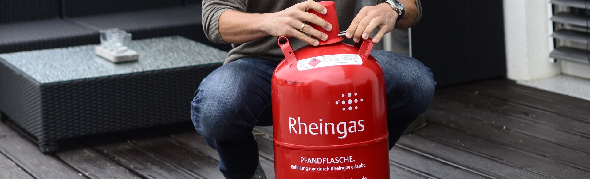 Mann hat eine rote mit Propan-Gas gefüllte Gasflasche von Rheingas gekauft und platziert sie auf der Terrasse.