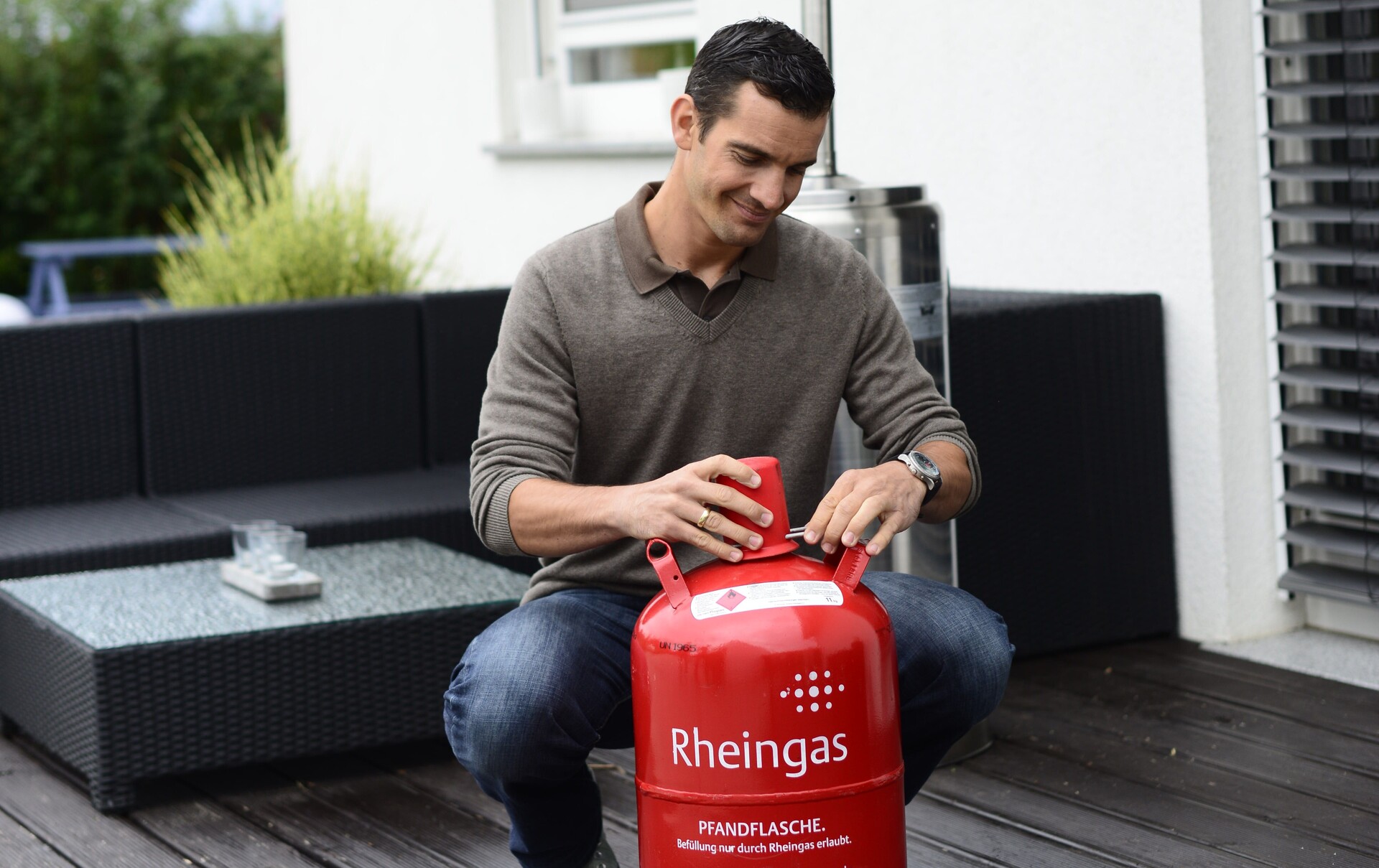 Mann sichert seine 11 kg Gasflasche von Rheingas mit roter Verschlusskappe, um sie richtig zu lagern.
