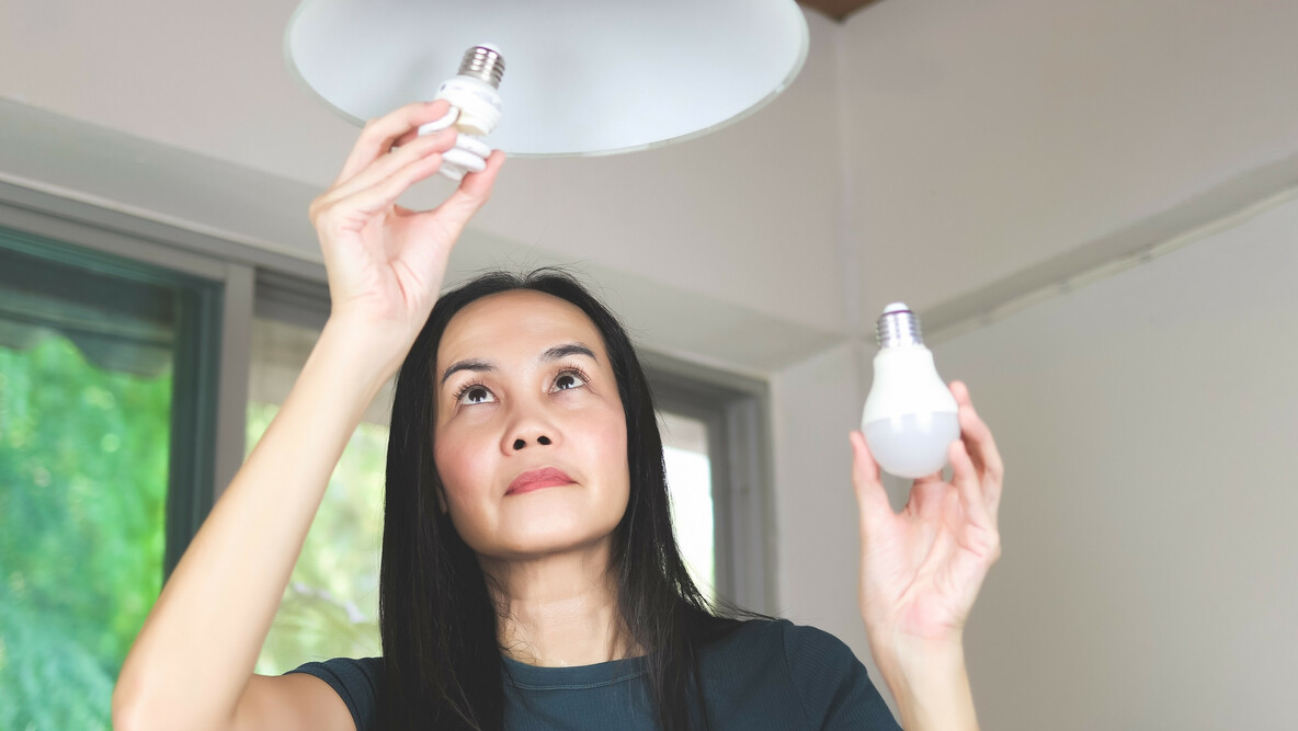 Frau wechselt Glühbirne gegen LED-Leuchte aus, um Energie zu sparen.