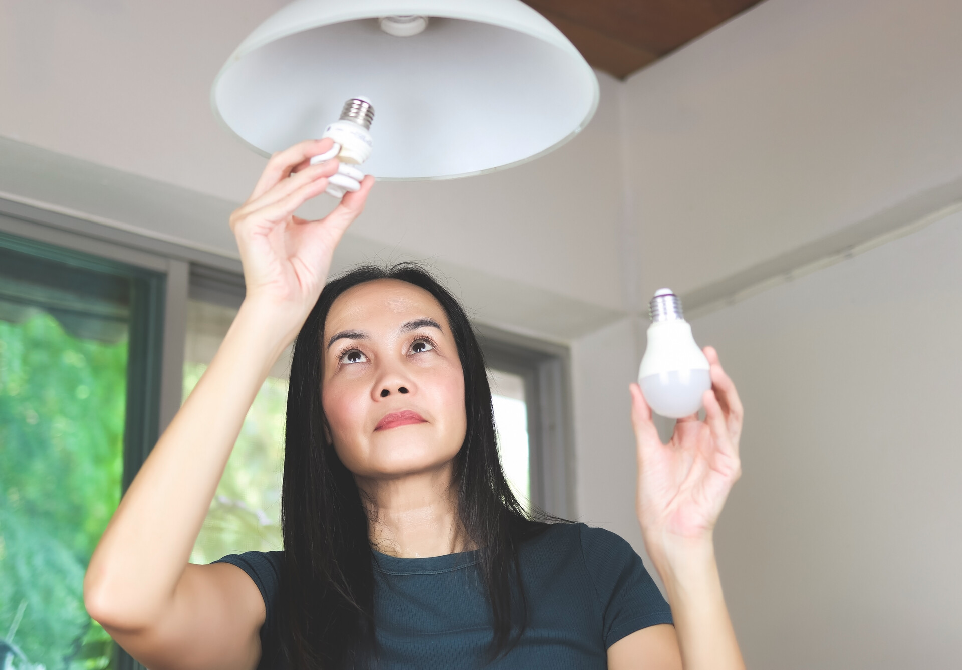 Frau wechselt Glühbirne gegen LED-Leuchte aus, um Energie zu sparen.
