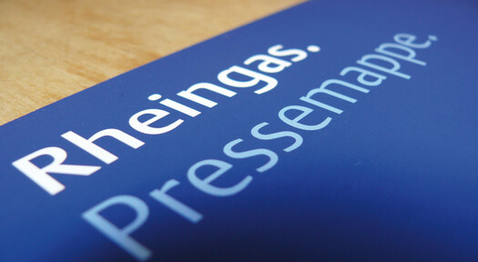 Blaue Rheingas Pressemappe auf einem Eichenholztisch.