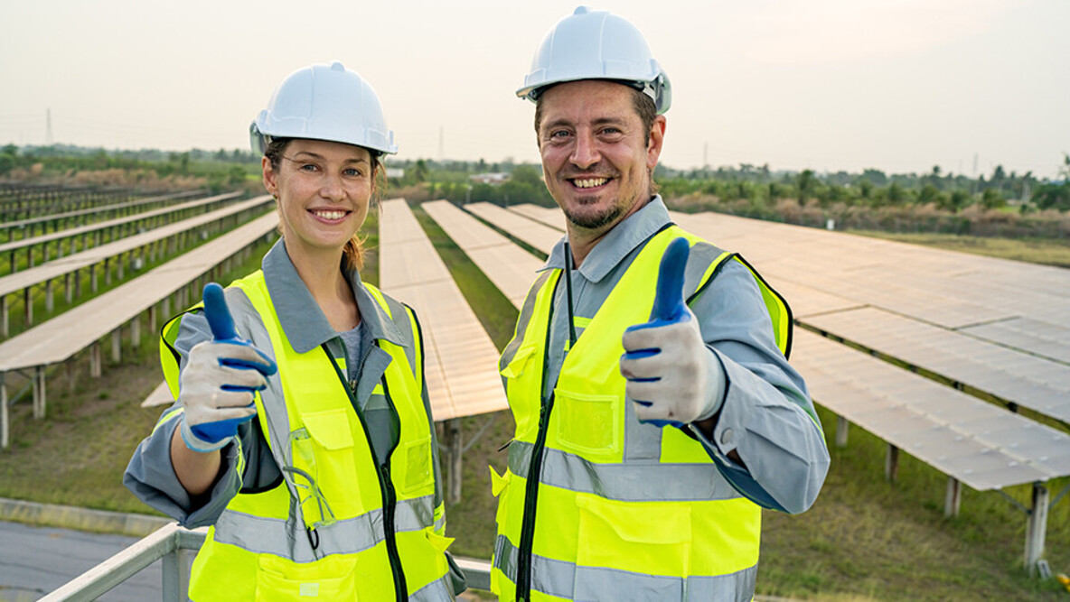 Eine Projektmanagerin für Elektroplanung und ein Projektmanager für Elektroplanung vor einer Photovoltaik-Großanlage.