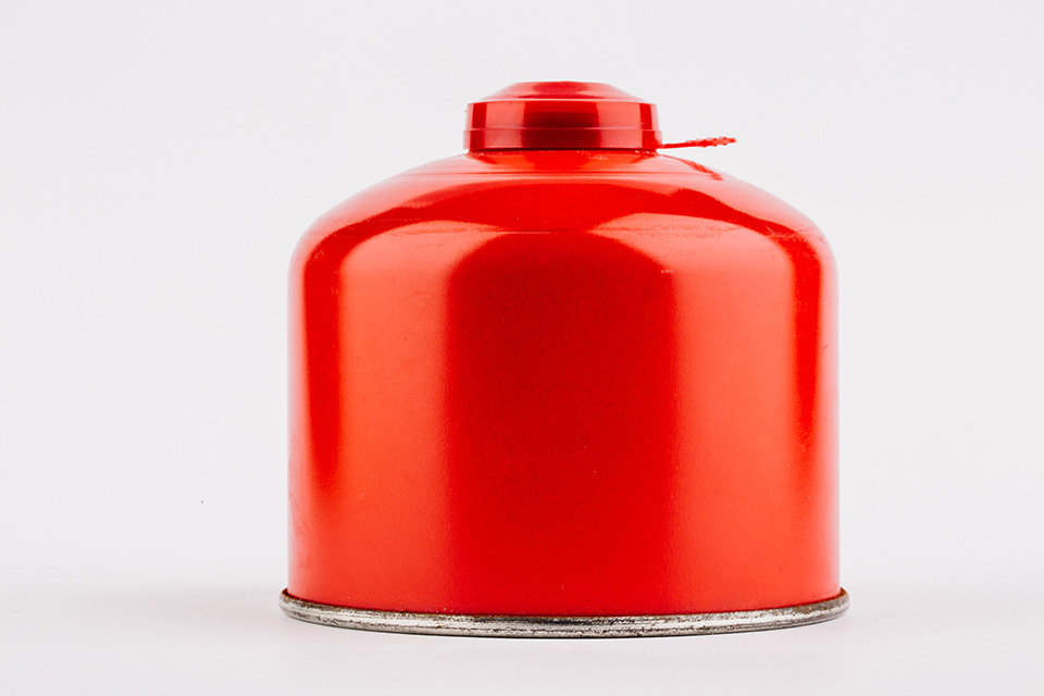Rote Gaskartusche mit Campinggas gefüllt vor einem neutralen Hintergrund.
